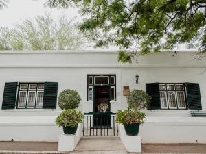 a white house with black shuttered windows and two potted plants at Karoo Cypress Guesthouse in Graaff-Reinet