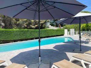 two umbrellas and chairs next to a swimming pool at ibis Nîmes Ouest - A9 in Nîmes