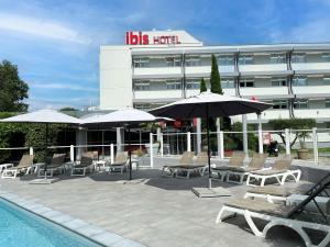 Una piscina con sillas y sombrillas frente a un edificio. en ibis Nîmes Ouest - A9, en Nimes