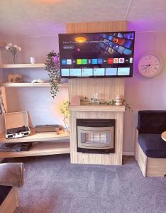 a living room with a tv above a fireplace at The Eden - Camber Sands Cosy Spacious Caravan in Camber