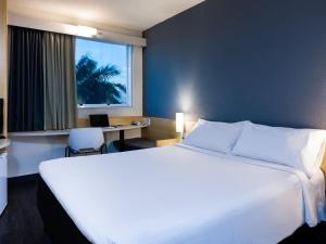 a hotel room with a large white bed and a desk at ibis Vitoria Aeroporto in Vitória