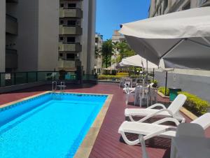 a swimming pool with white lounge chairs and an umbrella at Edifício Monte Carmel in Guarujá