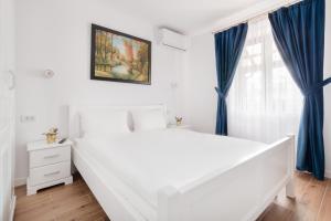 a white bedroom with blue curtains and a large window at Thermalis Groove in Baile Felix