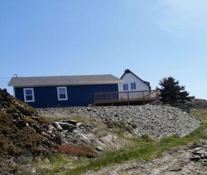 ein blaues Haus auf einem felsigen Hügel in der Unterkunft Oceanview Cottage in Twillingate