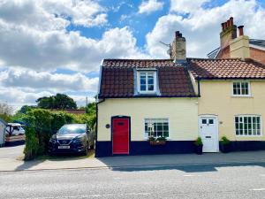 a white house with a red door and a car at Cherry Tree Cottage, Woodbridge in Woodbridge