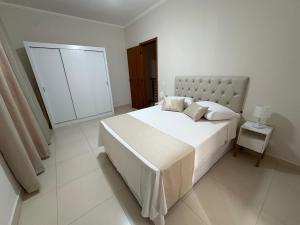 a white bedroom with a large bed and a lamp at Vila dos Pinheiros 2 in Serra Negra