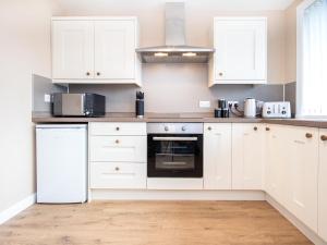 a white kitchen with white cabinets and appliances at Colbheinn Cottage in Brora +8 photos