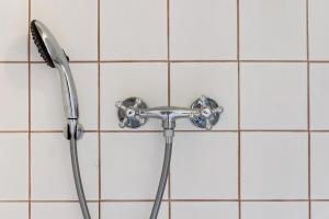 La salle de bains est pourvue d'une pomme de douche et de carrelage blanc. dans l'établissement Stråtækt feriehusidyl ved vandet, à Sønderborg 15 autres photos