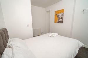 ein weißes Bett in einem Zimmer mit einem Bild einer Kuh in der Unterkunft Pitchside Comfort – 3-Bed Swansea Home in Morriston + 1 Foto