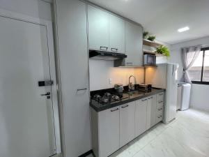 トレドにあるApe Harmonia novinho perto do Lago e Shoppingの白いキャビネット、シンク、冷蔵庫付きのキッチンが備わります。