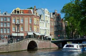 a boat on a river with buildings and a bridge at Manor Suite Amsterdam in Amsterdam