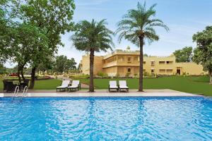 a pool with chairs and palm trees and a building at Syna Heritage Hotel in Khajurāho