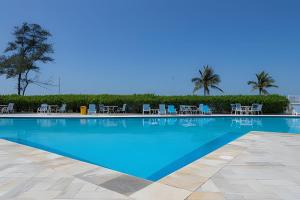 a large swimming pool with chairs and palm trees at Apart hotel a Beira Mar na praia do Recreio in Rio de Janeiro