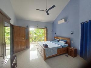 a bedroom with a bed with blue walls and a window at Roque's Place Goa in Betalbatim