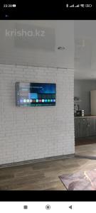 une télévision sur un mur de briques blanches dans une pièce dans l'établissement квартира Центр, à Semey
