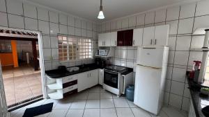 Elle comprend une petite cuisine avec des placards blancs et un réfrigérateur. dans l'établissement Casa de Temporada - Umuarama 2, à Uberlândia