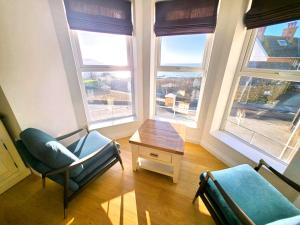 ein Wohnzimmer mit 2 Stühlen, einem Tisch und 2 Fenstern in der Unterkunft 1 Belmont Court in Woolacombe