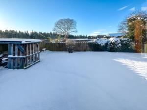 einen schneebedeckten Hof mit einem Zaun in der Unterkunft Lorien Cottage in Nethy Bridge