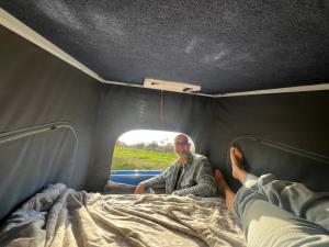 Un hombre sentado en una cama en un camión en rent a campervan vw t3 azul in Algarve Portugal, en Bicas