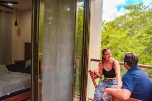 a man and a woman sitting on a balcony looking out a window at Loft Colibrí - Santuario Apartments in Chemuyil