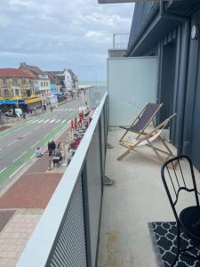 un balcon avec des chaises et un tableau blanc sur le côté d'un bâtiment dans l'établissement Entre Sable et Océan, appartement avec vue mer, à Fort-Mahon-Plage