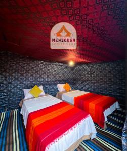 2 Betten in einem Zimmer mit Schild an der Wand in der Unterkunft Merzouga Deeper Camp in Merzouga