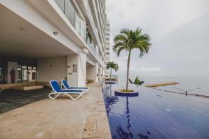 einem Pool mit Stühlen und einer Palme neben einem Gebäude in der Unterkunft SkyMar Luxury 27 in Cartagena de Indias