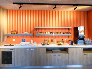 a kitchen with an orange wall and a counter with food at Ibis Budget La Rochelle Puilboreau in Puilboreau +64 photos
