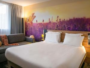 a bedroom with a large white bed and a couch at Novotel Antibes Sophia Antipolis in Valbonne