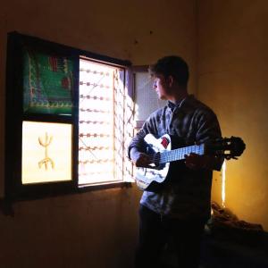 a young man playing a guitar in front of a window at Dar Nomad Tagounite in Zagora +40 photos
