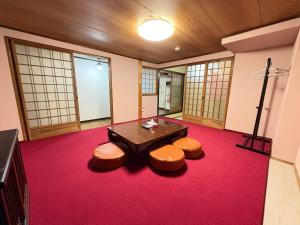 a room with a table and stools on a red carpet at Guesthouse すえ in Mashizume