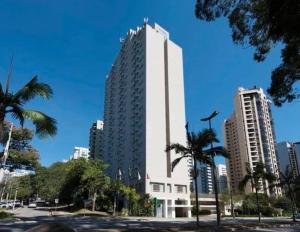 un grand bâtiment blanc dans une ville avec des palmiers dans l'établissement Prime Flat - Metrópolis Alphaville, à Barueri