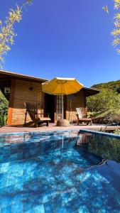 une piscine avec un parasol jaune et une maison dans l'établissement Cactus Chalés & Cabanas em lumiar, à Lumiar