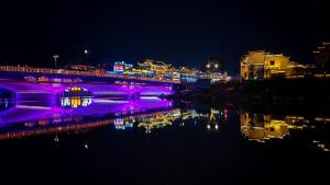 a bridge with purple lights over a river at night at GUI YUAN ZHEN PIN HOTEL,Approximately 3km away from the east gate of Zhangjiajie National Forest Park,Free Chinese western Breakfast,Free Self-Service Laundry , Attraction Tickets Serivce in advance,Free one-way shuttle service for 4 nights or more in Zhangjiajie