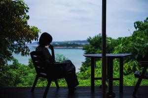 a woman sitting in a chair looking out at the water at Villa SACHIIBARU 浜辺の茶屋 の 宿 in Nanjo