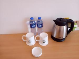 a table with two cups and a coffee pot and two water bottles at GreenTree Inn Shangrao Qianshan hekou old town Xinjiang longting shell hotel in Shangrao