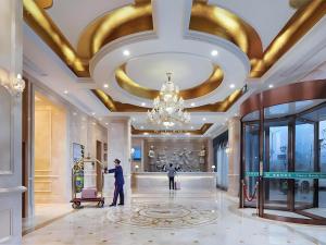 Ein Mann schiebt einen Gepäckwagen in einer Lobby mit einem Kronleuchter in der Unterkunft Vienna Hotel Anhui Xuancheng High-Speed Railway Station in Xuancheng