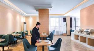 eine Frau steht an einem Tisch in einem Restaurant in der Unterkunft Vienna Hotel Taicang Shanghai East Road Landu Branch in Zhoujiating