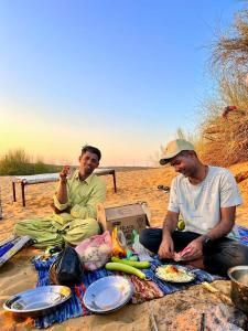 Dos hombres están sentados en la playa comiendo. en Hostel Camel Castle & Safari, en Jaisalmer