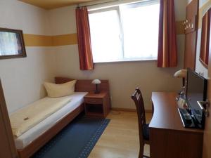 a small bedroom with a bed and a desk and a window at Hotel Heuschober in Friedrichshafen