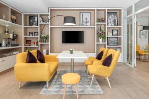 Sala de estar con 2 sillas amarillas y mesa en Citadines Montmartre Paris, en París