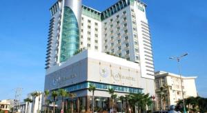 a large building with palm trees in front of it at Kaya Hotel in Phước Hậu