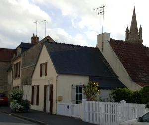 a white house with a black roof and a church at Maisoun Pequeux in Arromanches-les-Bains
