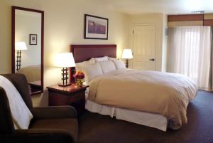 a hotel room with a bed and a chair and a mirror at Larkspur Landing Campbell-An All-Suite Hotel in Campbell
