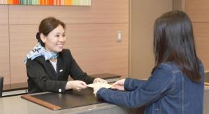 eine Frau gibt einer anderen Frau ein Stück Papier in der Unterkunft KEIKYU EX INN Keikyu Kawasaki-Station in Kawasaki