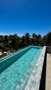 a swimming pool with turquoise tiles and palm trees at Patacho Brisa Mar - Triplex na Rota Ecológica dos Milagres in Pôrto de Pedras