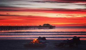 een groep mensen die rond een vuur op het strand zitten met een pier bij 5N-64 Beachfront On the Strand in Oceanside +18 foto's