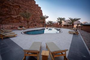 a swimming pool with tables and chairs next to a rock wall at Valley Resort in Wadi Rum +131 photos