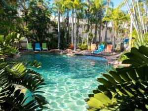 una piscina con sillas azules y palmeras en The Beach Motel Hervey Bay, en Hervey Bay