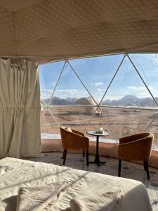 a bed and two chairs in a room with a view at RUM HORIZON BUBBlE LUXURY CAMP in Wadi Rum
